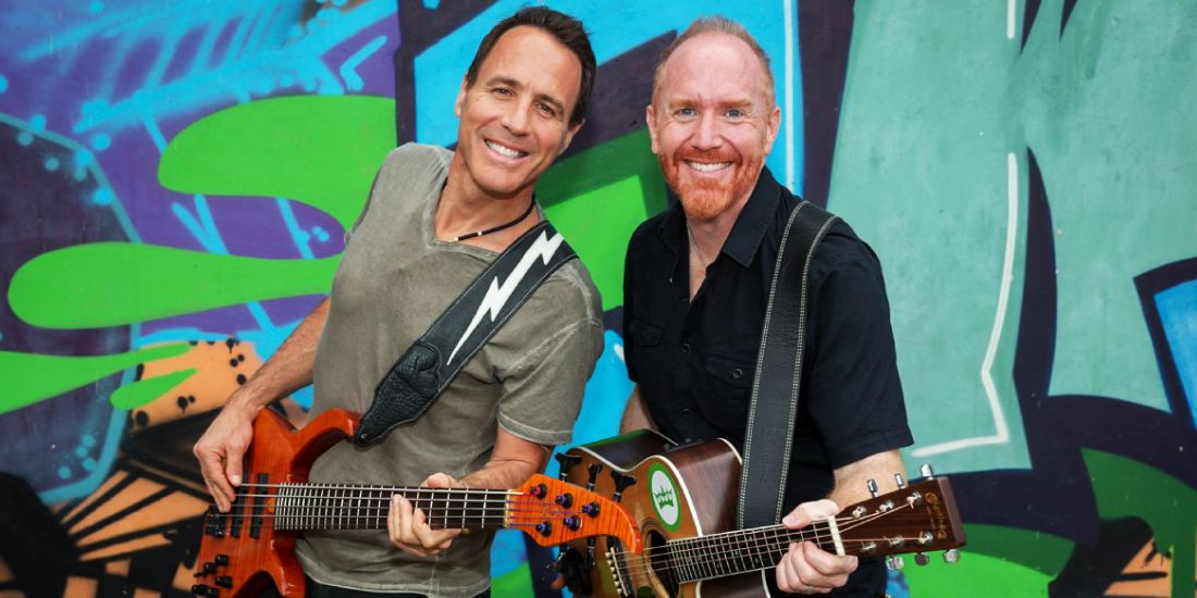 Mike Massé holding an acoustic guitar alongside Sterling Cottam holding a bass guitar against a colorful graffiti background.