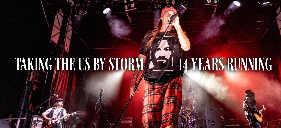 A Guns N' Roses tribute band performing live on a red-lit stage. The lead singer, wearing a plaid kilt, bandana, and graphic tee, sings into a microphone with a guitarist in a top hat to the right. Text reads: "Taking the US by Storm. 14 Years Running.