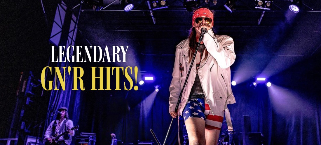 Close-up shot of a tribute band singer mimicking Axl Rose on a stage with purple lights, wearing a white jacket, bandana, sunglasses, and American flag shorts. Bold text on the left reads: "Legendary GN'R Hits!